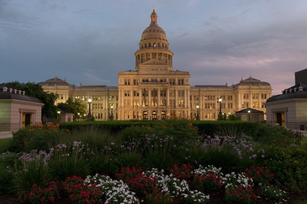 The Capitol Building in Austin Texas with colorful flower beds in the foreground lit up by street lights as the sun sets and a cloudy sky grows dark as dusk. ** Note: Visible grain at 100%, best at smaller sizes