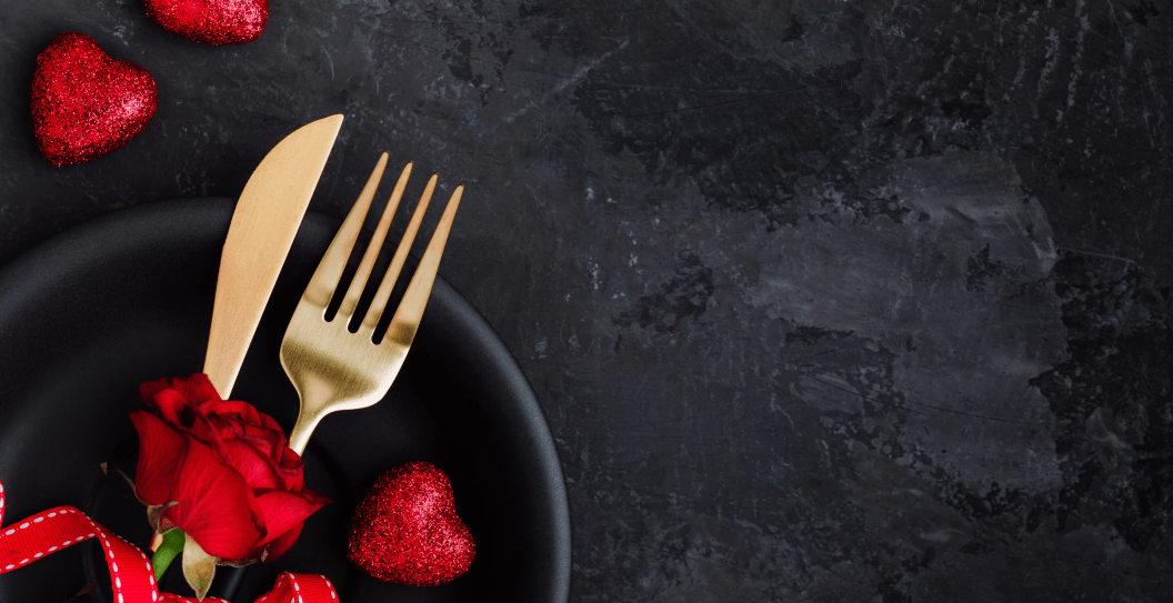 Valentine's Day table setting with plate, gold knife, fork, red rose, ribbon and hearts on dark background, top view, copy space. Valentines day background, holiday concept