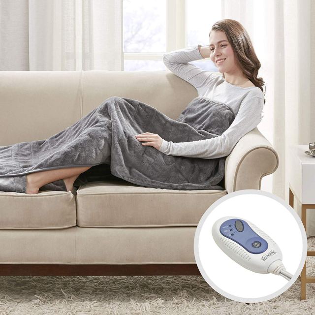 best heated throw blanket in color gray. woman is using it on a cream colored couch smiling