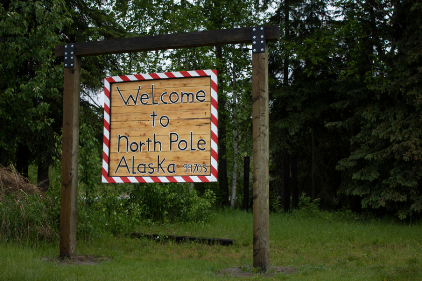 Homemade wooden sign with the words Welcome to North Pole Alaska with a candy cane frame surrounding the sign, hanging from wooden posts