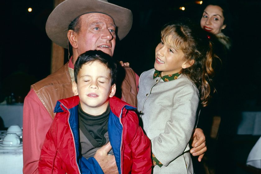 View of American actor John Wayne (1907 - 1979) with two of his children, son John Ethan and daughter Aissa Wayne, and, in the background, his wife, Peruvian-born actress Pilar Pallete, as they are photographed in an unspecified restaurant, 1967. Wayne is in costume (as Cole Thornton) for his role in 'El Dorado' (directed by Howard Hawks).