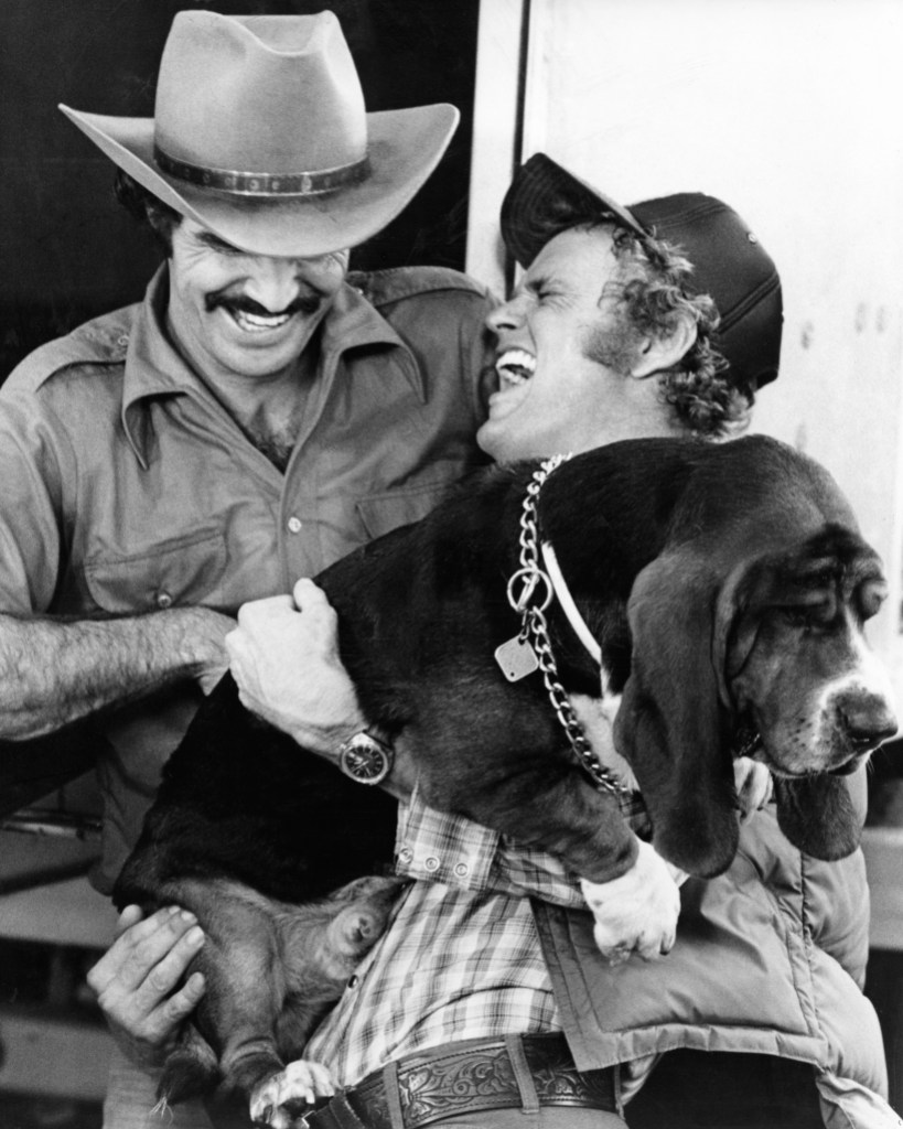 Actors Burt Reynolds as 'Bandit' and Jerry Reed as 'Cledus' with a Basset Hound dog in film 'Smokey and the Bandit', 1977. 