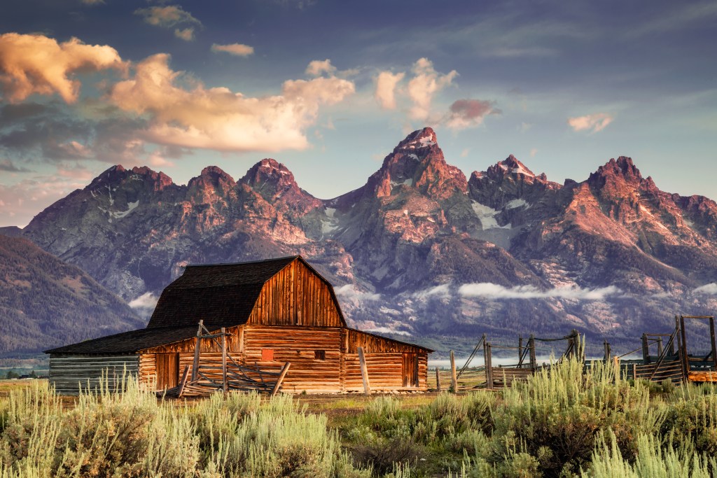 Early morning magenta light illuminates clouds and the Moulton Barn on Mormon Row at the foot of the Grand Tetons near Jackson, Wyoming, USA.