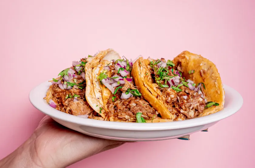 Delicious Mexican birria tacos with coriander and onion on top in a white plate held by one hand.