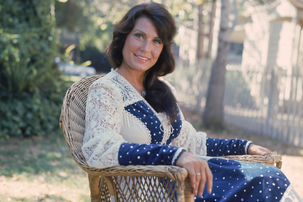 Portrait of American country music singer and musician Loretta Lynn sitting outdoors in a lace dress.