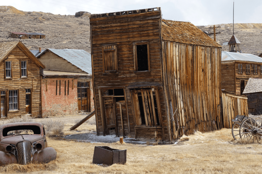 Rusty vintage car and idyllic wooden houses decay in the American wilderness after the gold rush. Scenic view of a ghost town in the Californian countryside slowly falling apart in rugged conditions.