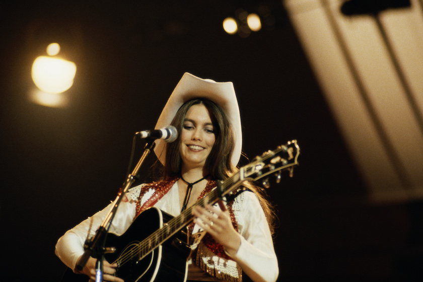 Emmylou Harris, U.S. singer-songwriter, playing the guitar while singing into a microphone during a concert, circa 1980. 