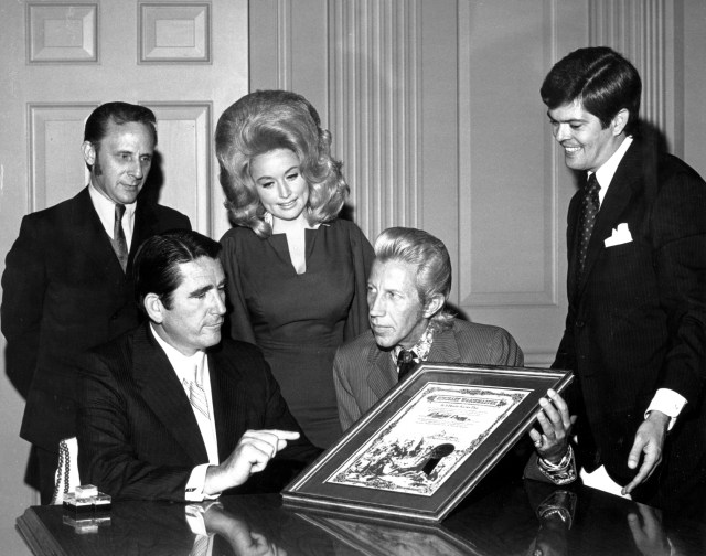 Country singer Porter Wagoner flanked by Dolly Parton and two other men presents a man with an "Honorary Wagonmaster" plaque in circa 1968.
