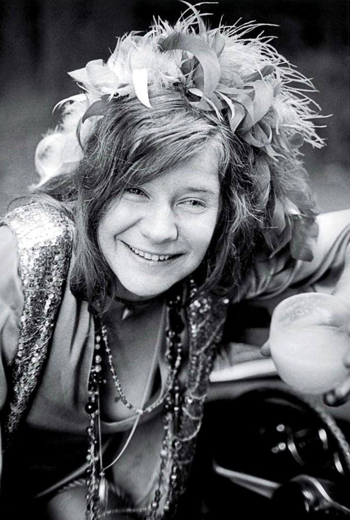 Photo of American singer Janis Joplin holding a glass in a car