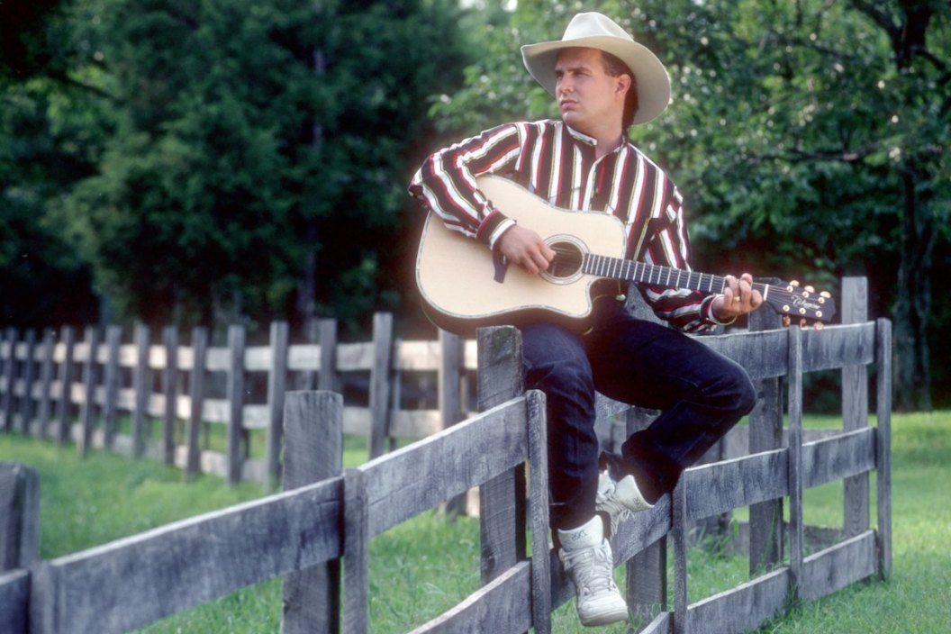 Country music star Garth Brooks poses for a portrait session on a fence wearing a cowboy hat and playing a Takamine acoustic guitar on August 15, 1991 in Nashville.
