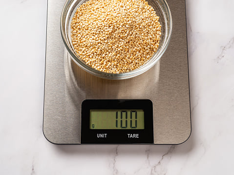 Raw dry quinoa in a glass bowl on a digital kitchen scale.