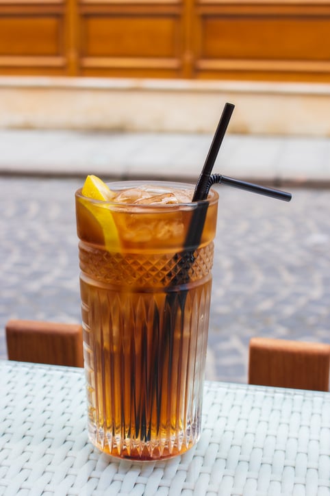 Long Island cocktail with two straws on table, isolated. Mixed alcoholic cocktail on table. Drinks in outdoor bar. Summer party. Cool alcoholic cocktails. Refreshing aperitif. Long Island in sidewalk cafe. City lifestyle concept.