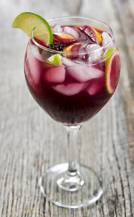 A large wine glass full of ice cold, refreshing red sangria. It is filled with a delicious variety of healthy fresh fruit including blackberries, limes, oranges and peaches. The background is a rustic piece of old weathered wood. Selective focus was used when creating this image.
