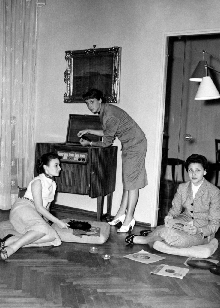 Girls relaxing by listening to a record player. 1950s 