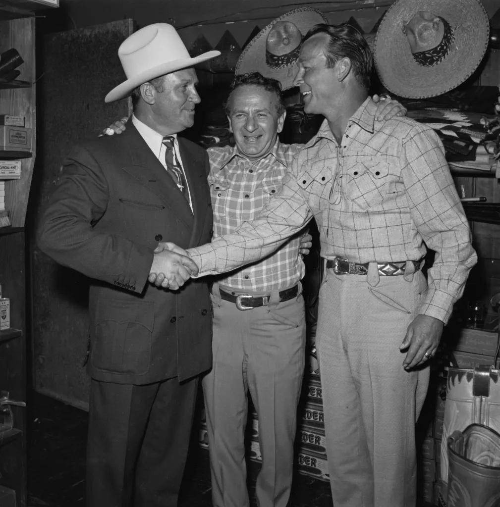 From left to right, actor and singer Gene Autry (1907 - 1998), tailor Nudie Cohn (1902 - 1984) and actor and singer Roy Rogers (1911 - 1998) at a party for Cohn and various Western stars, USA, circa 1960. Nudie Cohn designed decorative suits covered in rhinestones, known as 'Nudie' suits. 