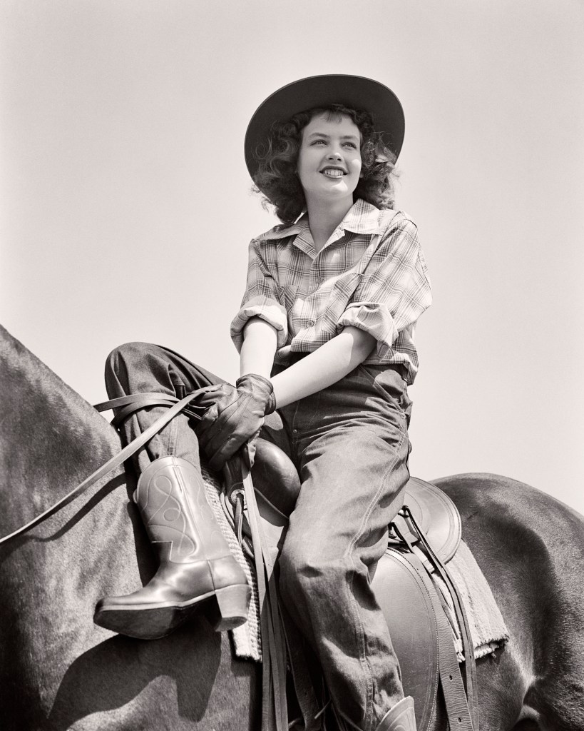 1940s Teenage Girl Wearing Western Clothes Cowboy Boots Plaid Shirt And Hat In Relaxed Pose Sitting On Horse With Western Saddle.