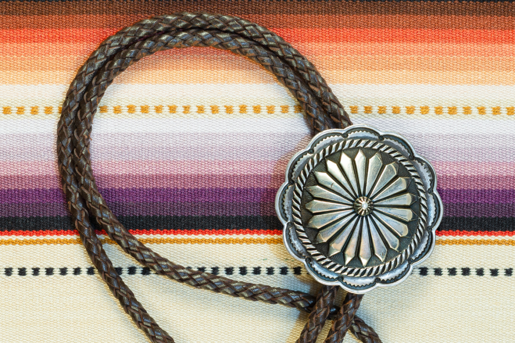 Vintage Sterling Silver Bolo Tie with Concho and Silver Tips on colorful southwestern hand woven fabric.