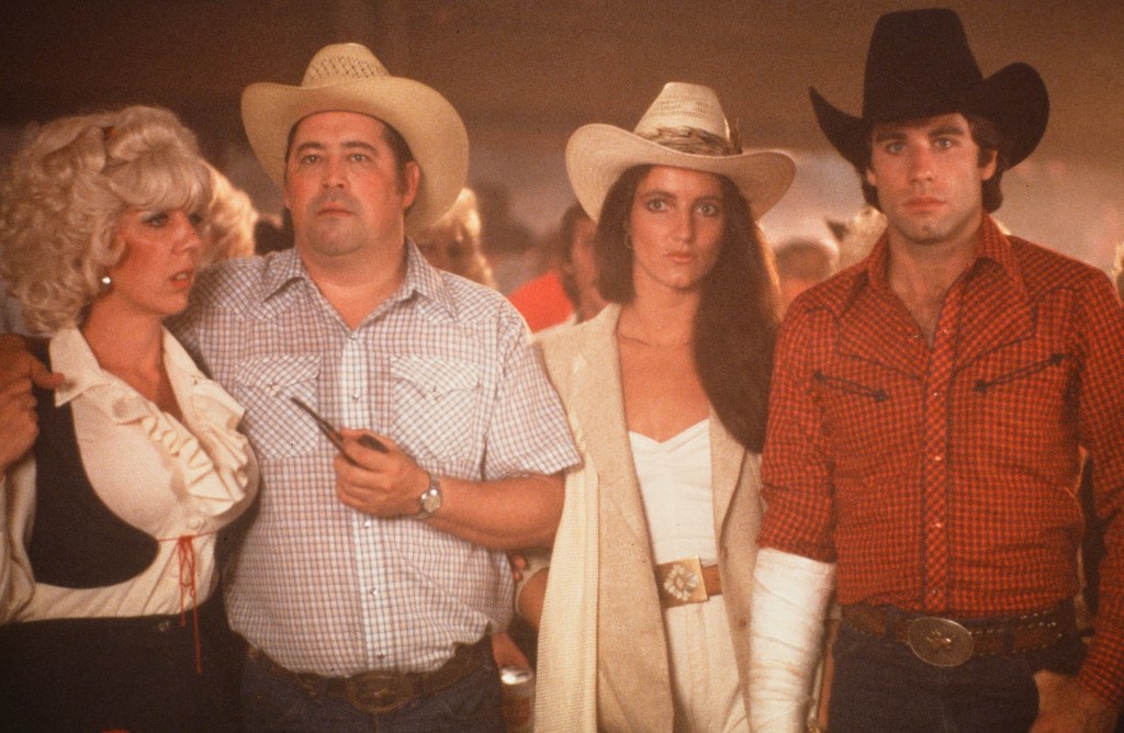 Actors Barry Corbin with actress Madolyn Smith Osborne and John Travolta stand in a scene during the Paramount Pictures movie 'Urban Cowboy" circa 1980. 