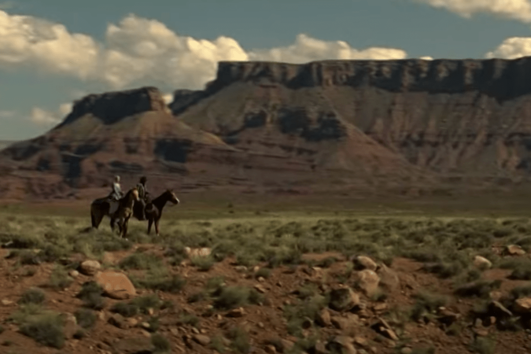 Two riders on horseback overlooking the view of the mountains in a scene from 'Westworld'