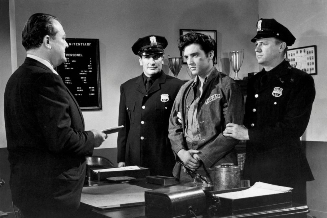 Elvis Presley is held by guards Carl Sax (left) and Hubi Kearns (right) as Warden Hugh Sanders prepares to sentence Elvis for creating a disturbance in prison in a scene from the 1957 film Jailhouse Rock.