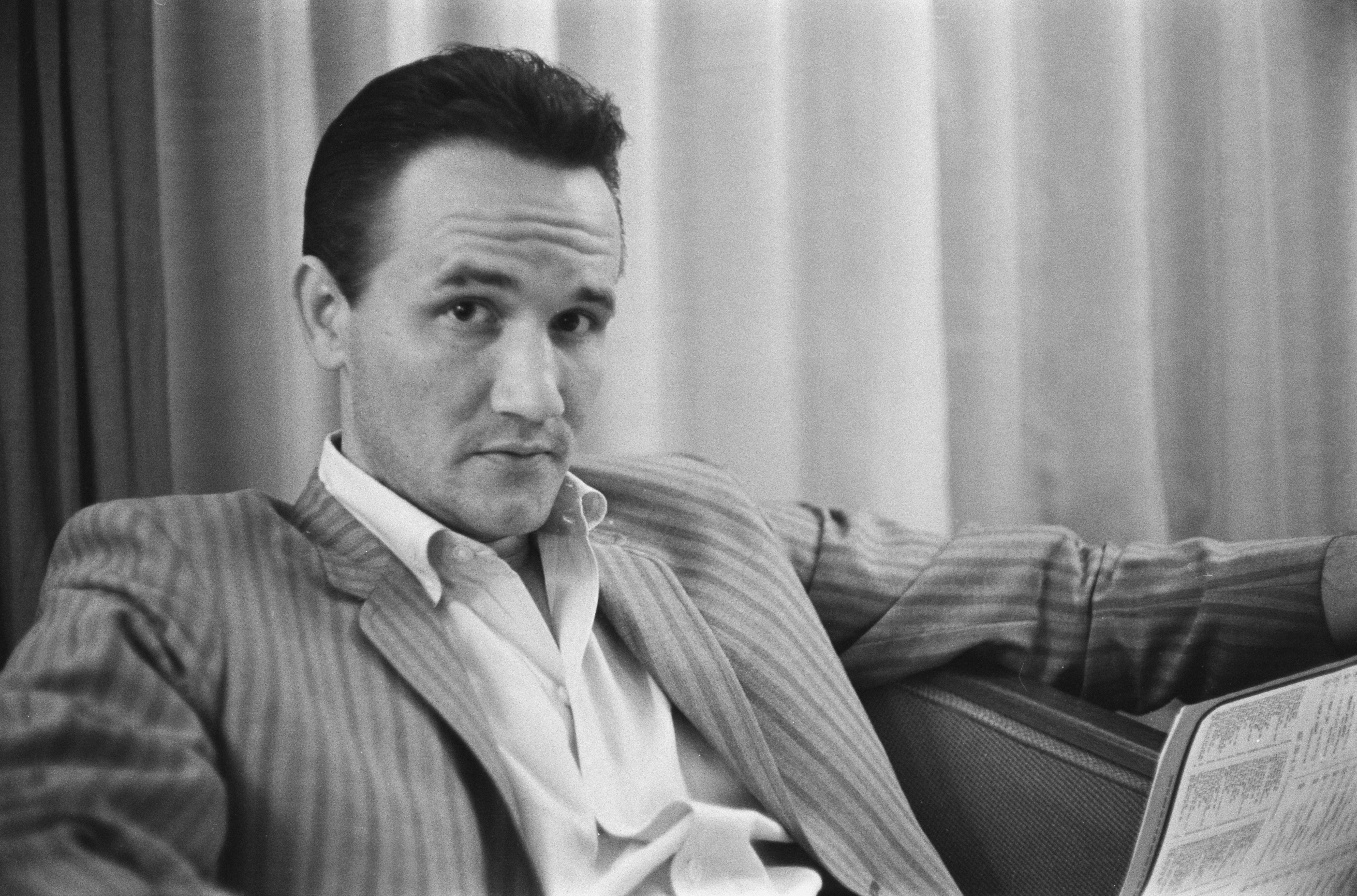 American singer-songwriter Roger Miller (1936-1992) wearing a striped blazer over a white shirt with the collar open, location unspecified, 1964. 