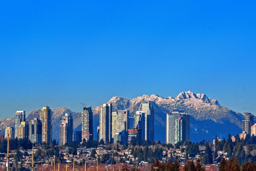 New residential area of high-rise buildings in the city of Burnaby, construction site in the center of the city against the backdrop of snow covered mountain range and blue sky