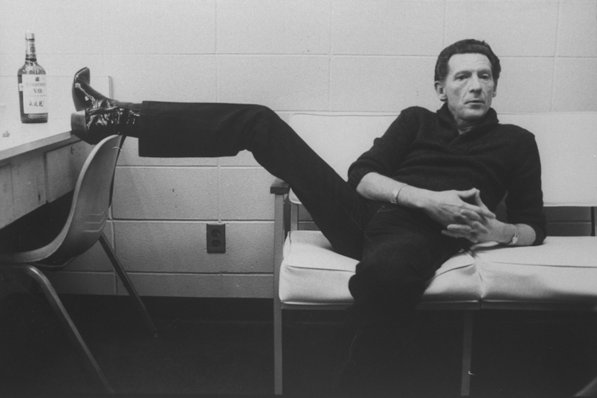 Singer Jerry Lee Lewis lounging on couch w. one foot up on dressing table next to a bottle of Seagram's V.O. whiskey in dressing room at Performing Arts Center.