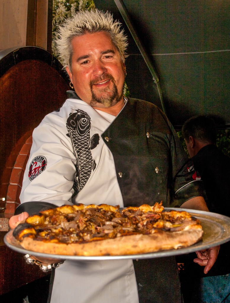 HEALDSBURG, CA - MARCH 24: Celebrity chef and TV Food Network star, Guy Fieri, poses with a freshly baked pizza at Charlie Palmer's Pigs & Pinot charity event held on March 24, 2012, in Healdsburg, California. Charity wine and food events have become a cottage industry, raising tens of millions of dollars each year for local and national non-profit organizations.