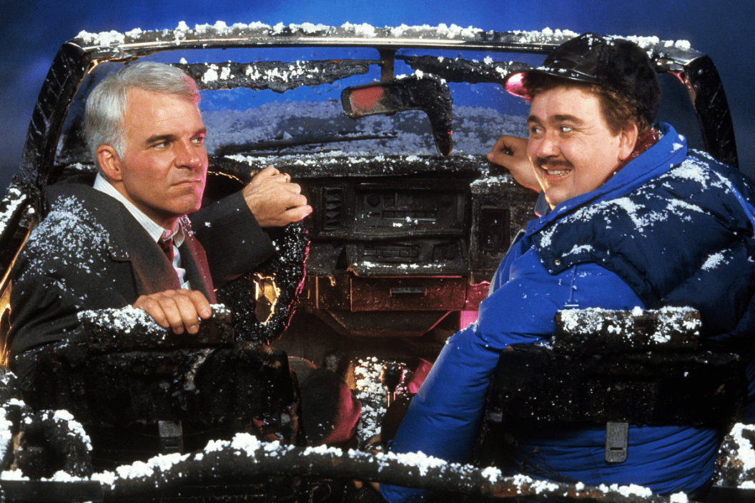 Steve Martin and John Candy sit in a destroyed car in a scene from the film 'Planes, Trains & Automobiles', 1987
