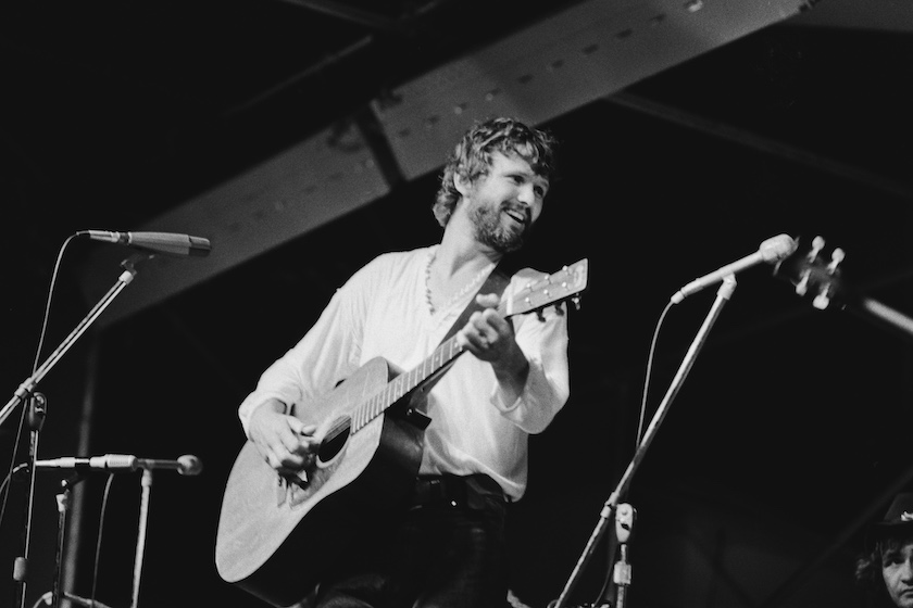 American singer-songwriter and actor Kris Kristofferson, wearing a white v-neck top, playing an acoustic guitar as he performs live at the Schaefer Music Festival, held at the Wollman Rink in Central Park in New York City, New York, 9th August 1971. 