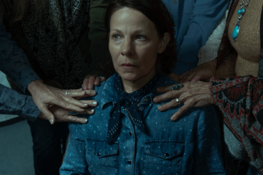 Lili Taylor (Cecilia Abbott) sits in a chair surrounded by other women resting their hands on her shoulders