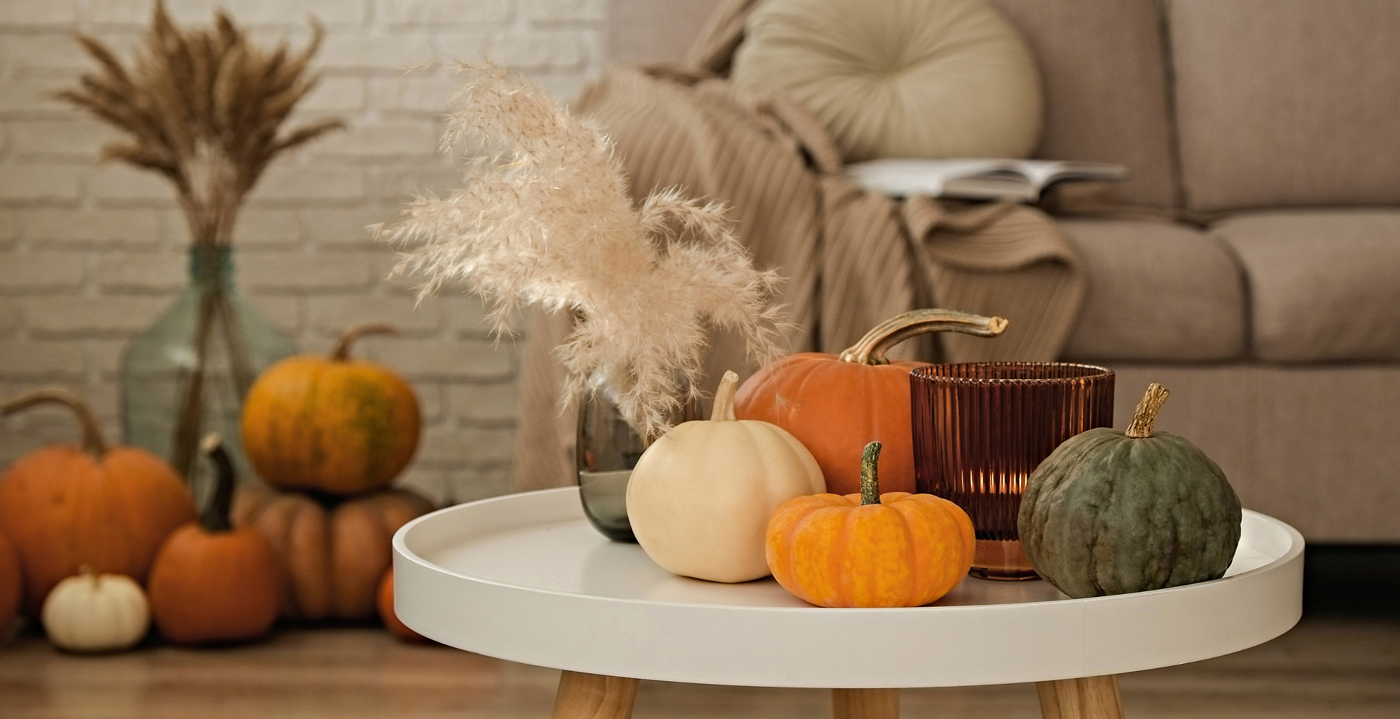 Bunch of pumpkins of different kinds, shapes and colors on the floor and a table near the couch of a living room. Symbol of autumnal holidays with a lot of copy space for text, close up, background.