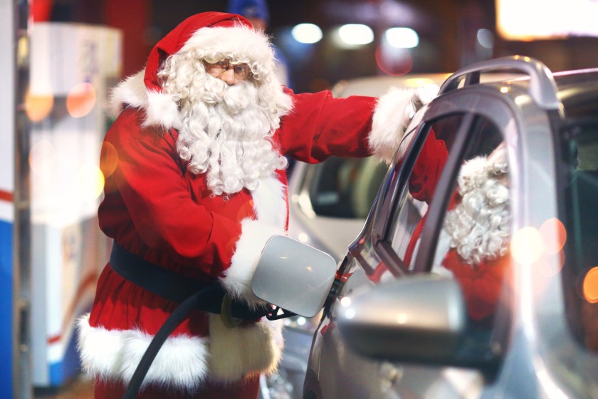 Santa Claus at gas station filling up the tank of his car. He's modern Santa and he drives SUV, raindeer called in sick. The Santa is looking at camera. Night shot.
