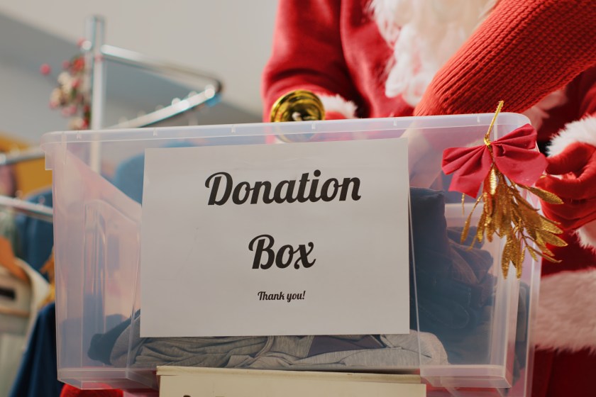 Close up shot of donation box in fashion shop set up for humanitarian help during Christmas holiday season. Worker dressed as Santa Claus collecting unneeded clothes from generous clients