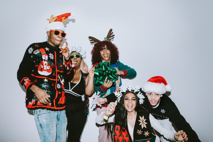 A group of young adult friends gather at a home for Christmas celebration over the holiday, dressed to fit the occasion with various Christmas accessories and ugly sweaters. They pose for some photos, direct camera flash.