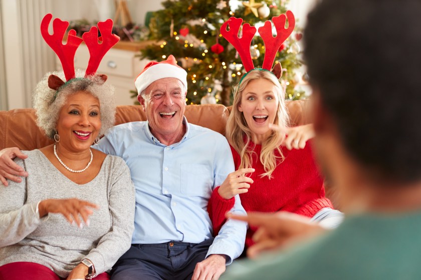 Adult Family Sitting On Sofa Playing Game Of Charades At Christmas Together