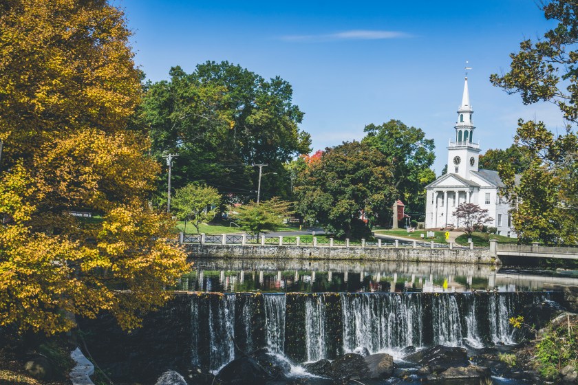 Milford, town in Connecticut. View of white church and waterfall surrounded by trees.