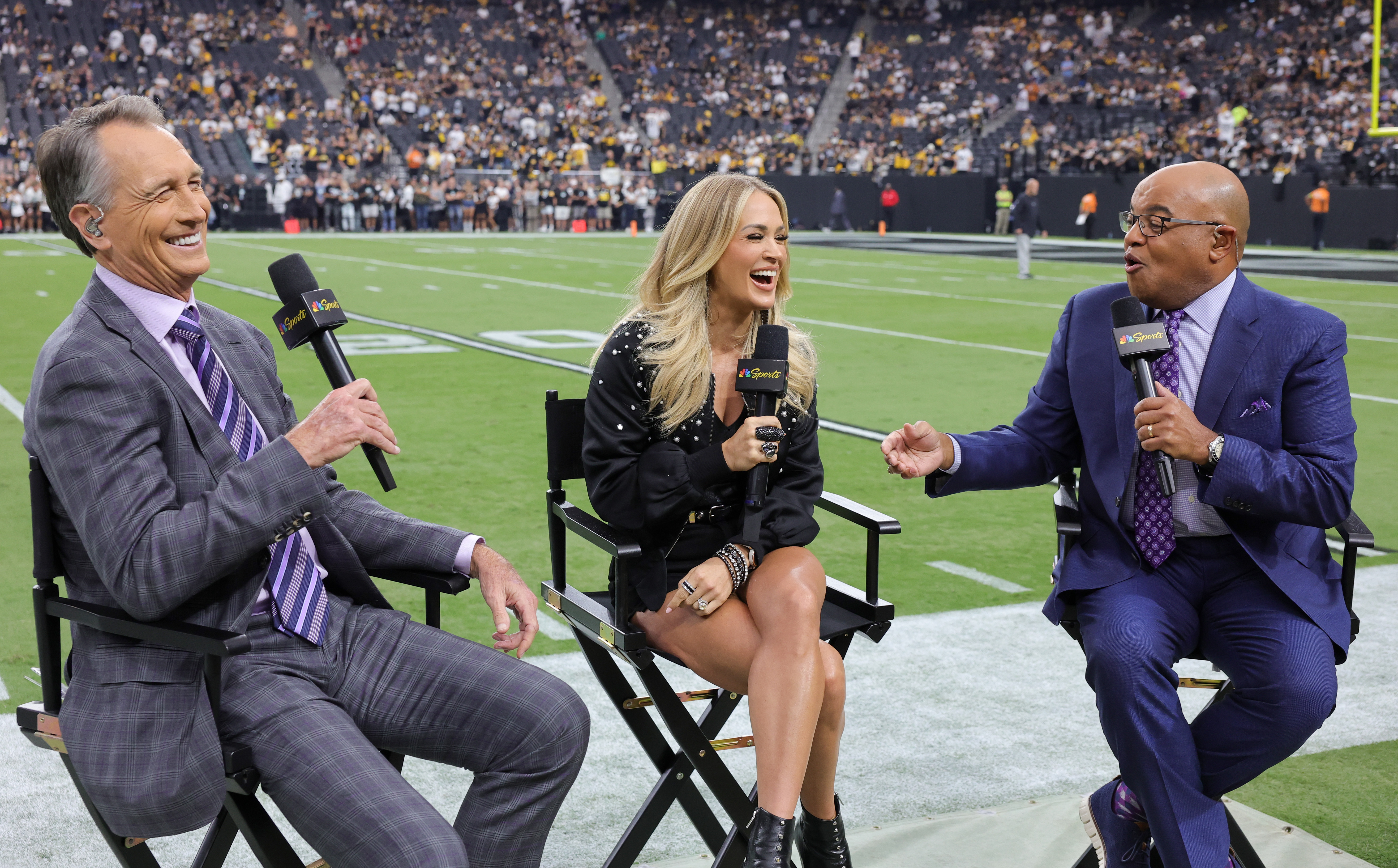LAS VEGAS, NEVADA - SEPTEMBER 24: (L-R) NBC Sunday Night Football color commentator Cris Collinsworth, recording artist Carrie Underwood and NBC Sunday Night Football play-by-play announcer Mike Tirico talk before a game between the Pittsburgh Steelers and the Las Vegas Raiders at Allegiant Stadium on September 24, 2023 in Las Vegas, Nevada. The Steelers defeated the Raiders 23-18.