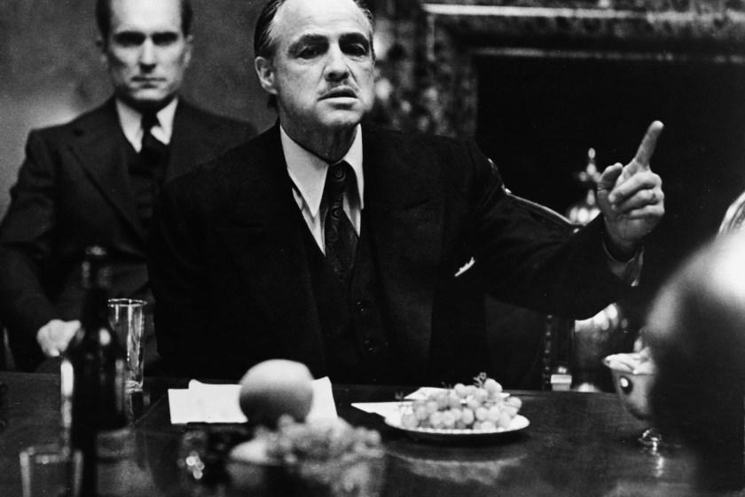 American actor Marlon Brando gestures at a table while American actor Robert Duvall sits behind him in a still from the film, 'The Godfather,' directed by Francis Ford Coppola and based on the novel by Mario Puzo.