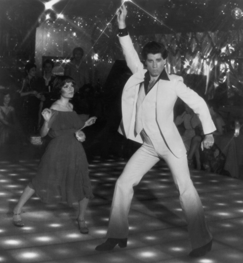 John Travolta as Tony Manero in his famous disco-dancing pose in Saturday Night Fever (1977). His dance partner is actress Karen Lynn Gorney.