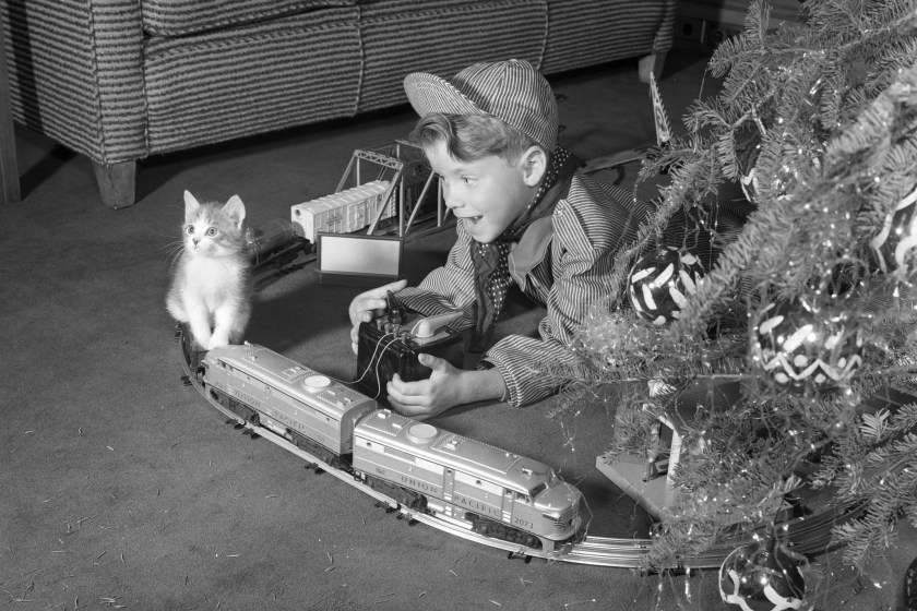 1950s BOY IN ENGINEER OUTFIT WITH KITTEN PLAYING WITH ELECTRIC TRAIN BY CHRISTMAS TREE (Photo by Debrocke/ClassicStock/Getty Images)
