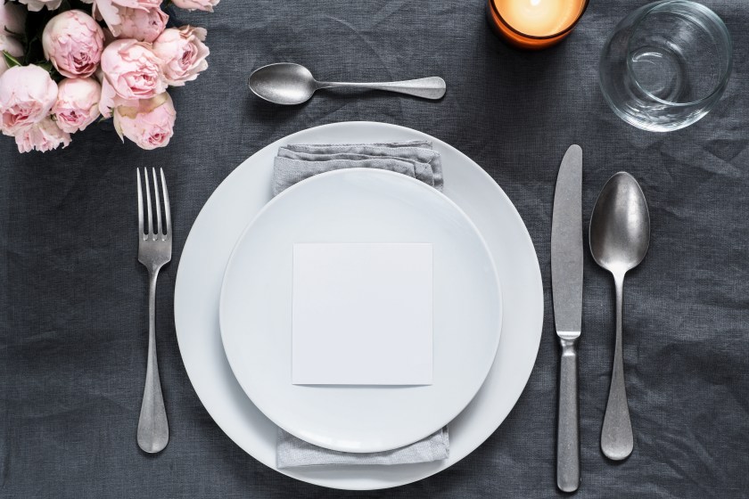 Menu, wedding invitation mock up. Beautiful table setting on gray linen tablecloth. Festive table setting for wedding dinner with pink spray roses and cabdle. Holiday dinner, white plates. Copy space