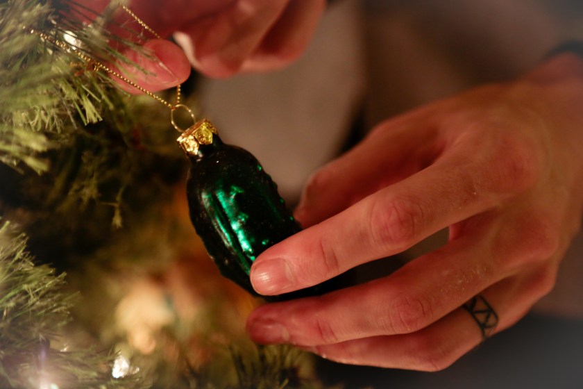 A man hanging up a unique pickle ornament on a Christmas tree