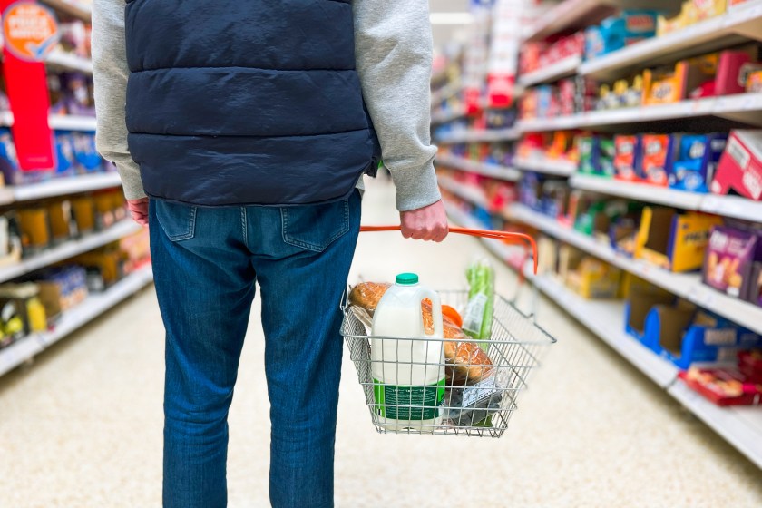Man holding shopping basket with bread and milk groceries in supermarket