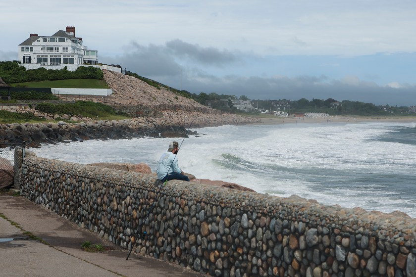 Westerly, RI - August 22: A man fishes at the Watch Hill Lighthouse for stripped bass with home of Taylor Swift in the background during the eye of the Tropical Storm Henri in Westerly, RI on Aug. 22, 2021.