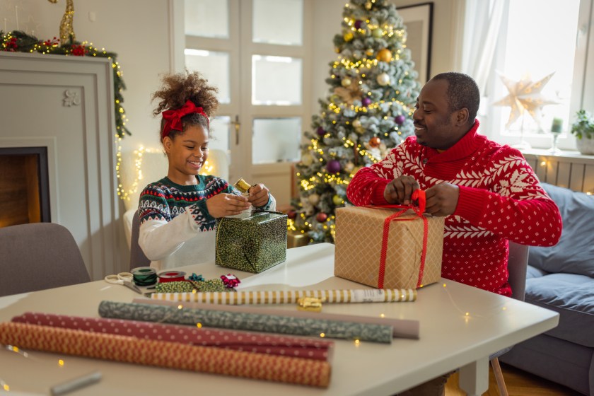 Father and daughter wrapping Christmas gifts. They are wearing Christmas sweater and having fun.