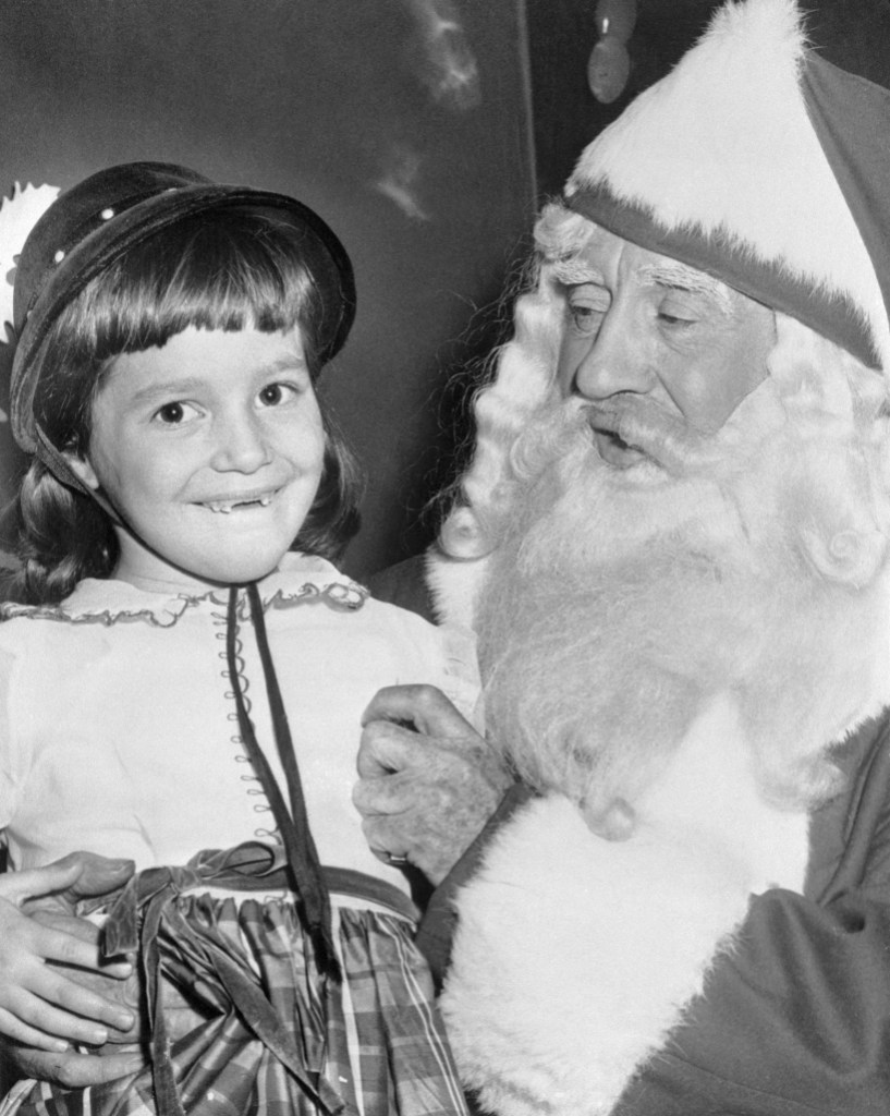Girl missing two front teeth talking to Santa Claus.