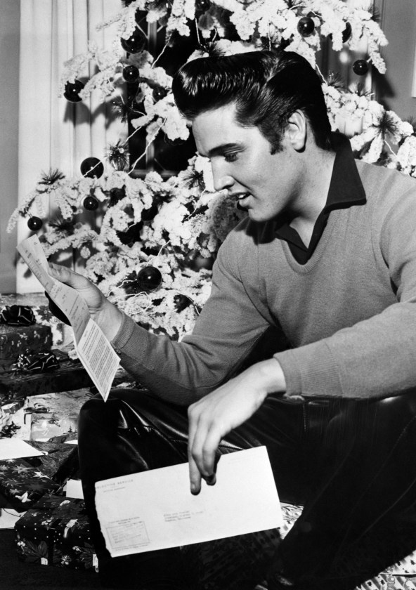 Elvis Presley reads his draft notice in front of a Christmas tree.