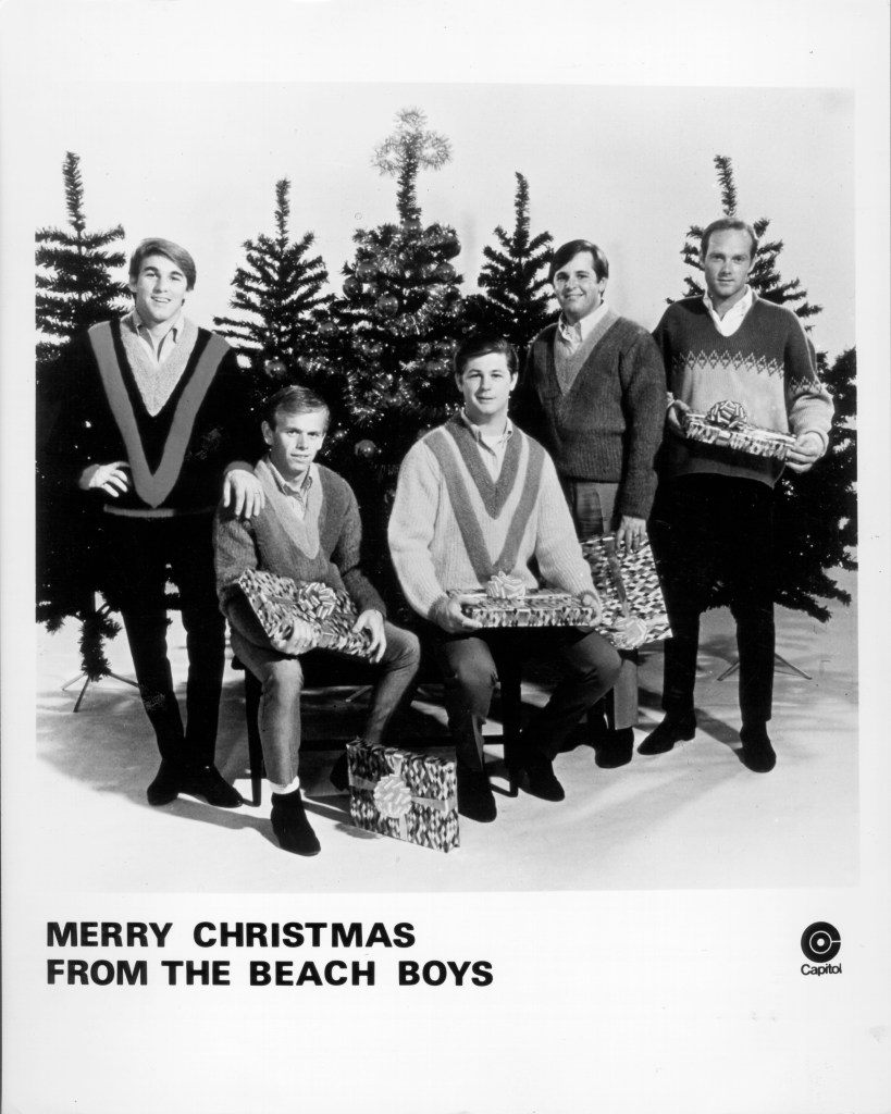 Rock and roll band "The Beach Boys" pose for a portrait in front of some Christmas trees holding presents in circa 1964. 