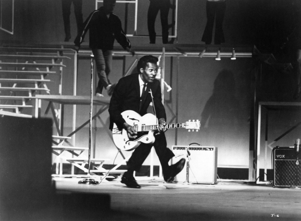 Rock and roll guitarist Chuck Berry performs his "duck walk" as he plays his electric hollowbody guitar.